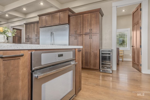 kitchen with wine cooler, stainless steel appliances, light wood-style floors, beam ceiling, and coffered ceiling