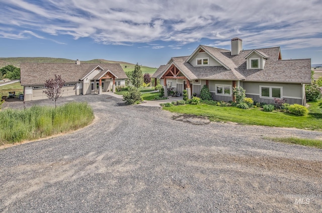 craftsman-style house with a chimney, gravel driveway, a garage, and roof with shingles