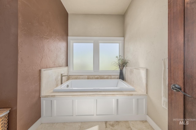 bathroom featuring a bath, baseboards, and a textured wall