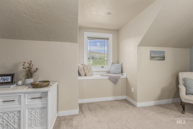 sitting room with a textured ceiling, vaulted ceiling, light colored carpet, and baseboards