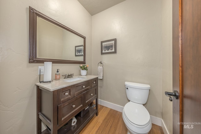 bathroom with wood finished floors, toilet, vanity, and baseboards