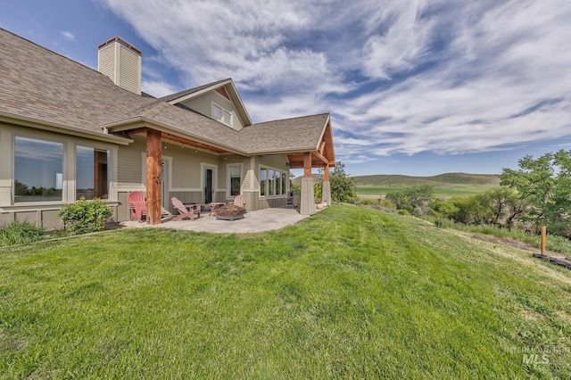 back of property featuring a patio area, a fire pit, a yard, roof with shingles, and a chimney