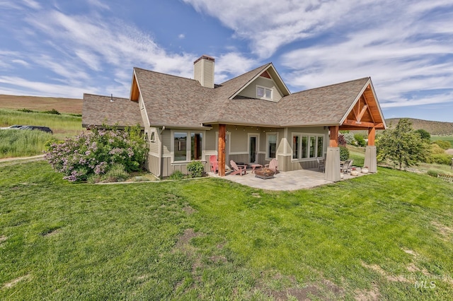 back of house with a patio, a chimney, a yard, and a shingled roof