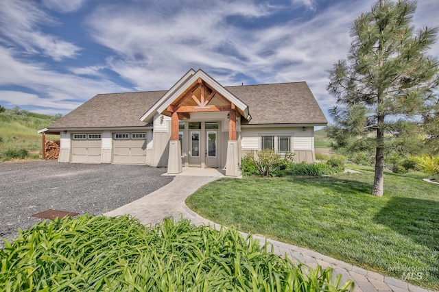 view of front of home featuring a front yard, a shingled roof, gravel driveway, and a garage