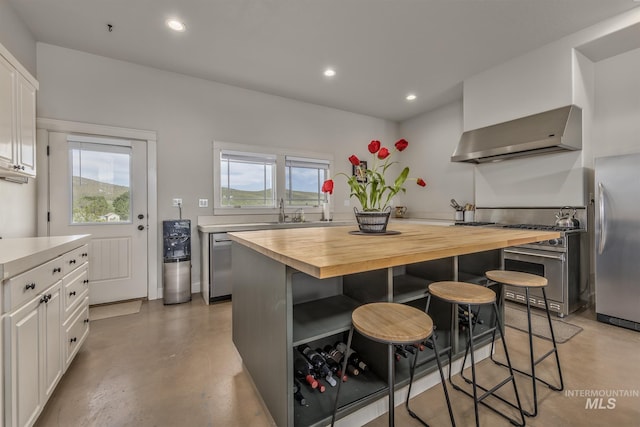 kitchen featuring freestanding refrigerator, ventilation hood, butcher block countertops, concrete flooring, and a breakfast bar