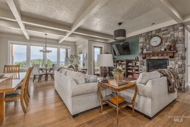 living room with a chandelier, light wood-style flooring, a textured ceiling, beamed ceiling, and a fireplace
