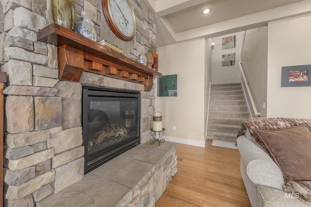 living area with a fireplace, wood finished floors, stairway, baseboards, and a raised ceiling