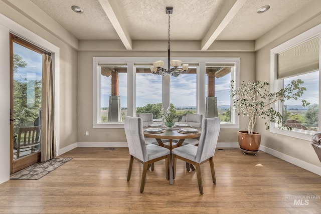 dining room with beamed ceiling, a textured ceiling, a chandelier, light wood-style floors, and healthy amount of natural light