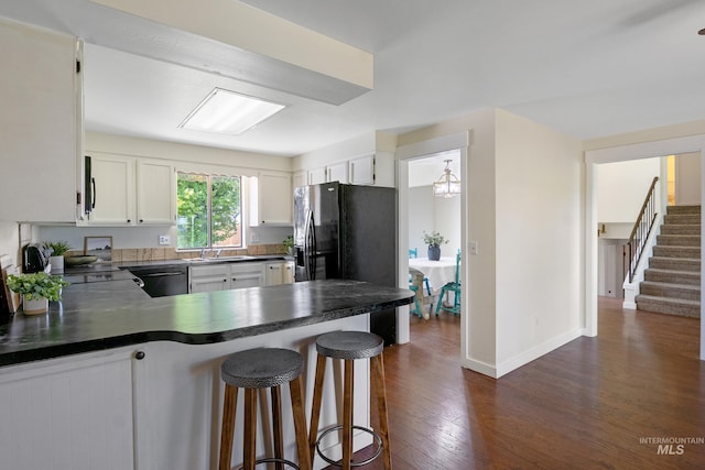 kitchen featuring dark countertops, a sink, black refrigerator with ice dispenser, a peninsula, and dark wood-style floors