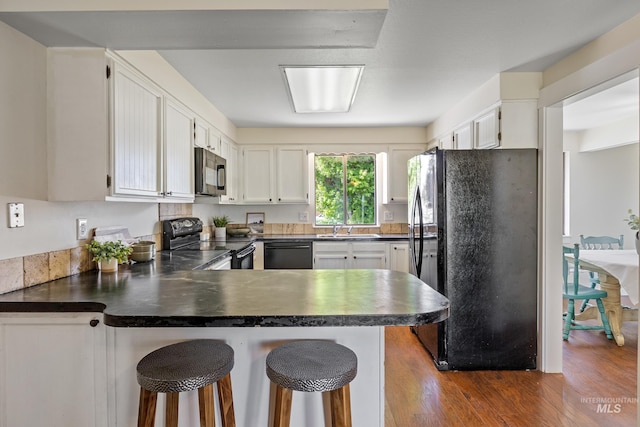 kitchen featuring a peninsula, dark countertops, dark wood-style floors, a sink, and black appliances