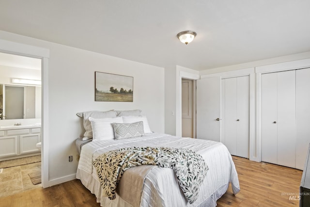 bedroom with a sink, multiple closets, ensuite bathroom, and light wood finished floors