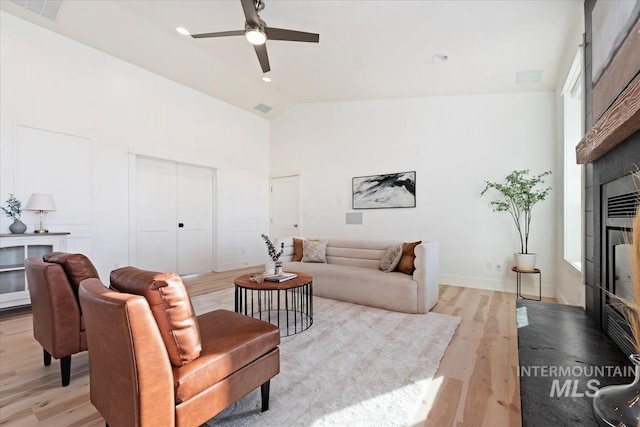 living room with ceiling fan, vaulted ceiling, a tile fireplace, and light hardwood / wood-style flooring