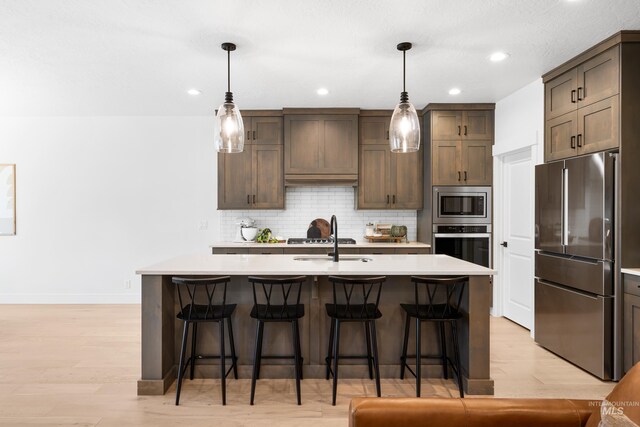 kitchen with appliances with stainless steel finishes, light countertops, a sink, a kitchen breakfast bar, and recessed lighting