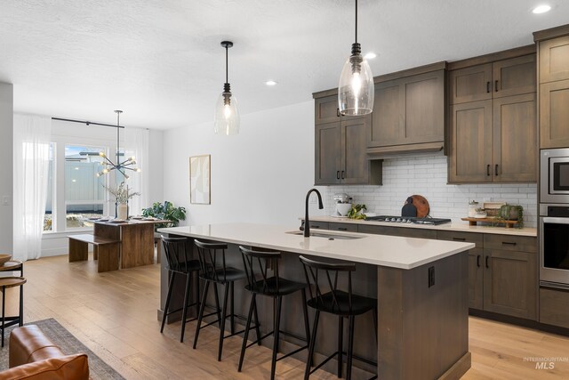 kitchen with a sink, decorative backsplash, an island with sink, light countertops, and light wood-style floors