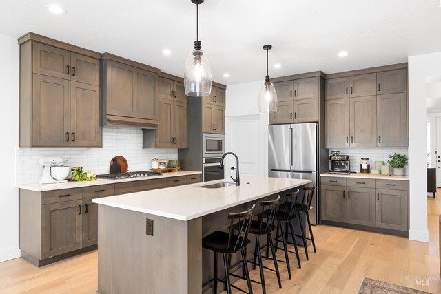 kitchen featuring a sink, stainless steel appliances, light wood-style floors, decorative backsplash, and light countertops