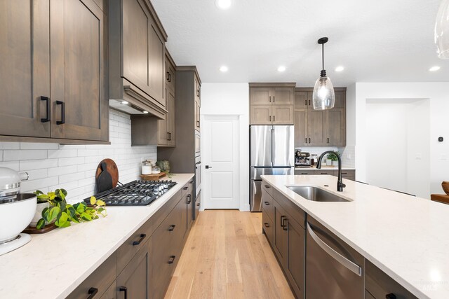 kitchen with a sink, appliances with stainless steel finishes, pendant lighting, light wood-style floors, and backsplash