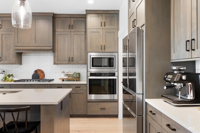 kitchen featuring appliances with stainless steel finishes, light countertops, decorative backsplash, light wood-style floors, and recessed lighting