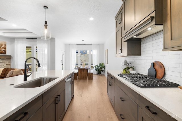 kitchen with a sink, appliances with stainless steel finishes, decorative backsplash, light wood-style floors, and hanging light fixtures