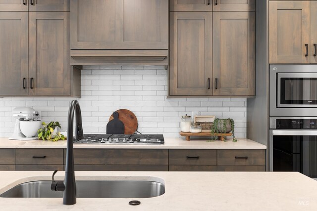 kitchen with a sink, decorative backsplash, appliances with stainless steel finishes, and dark brown cabinetry