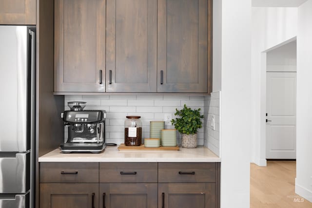 bar area with freestanding refrigerator, tasteful backsplash, and light wood-style floors