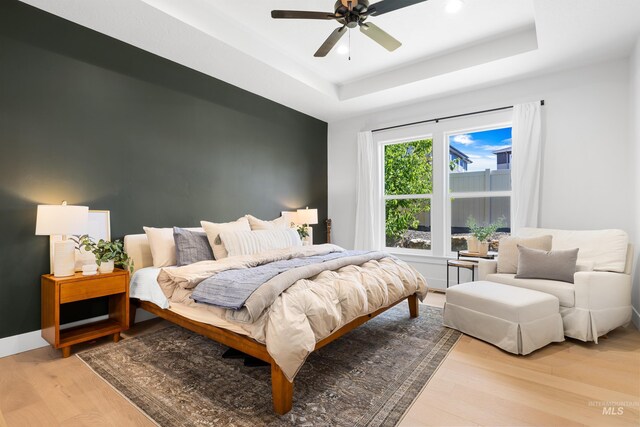 bedroom featuring light wood-type flooring, a raised ceiling, recessed lighting, ceiling fan, and baseboards