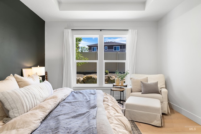 bedroom featuring wood finished floors, baseboards, and a raised ceiling