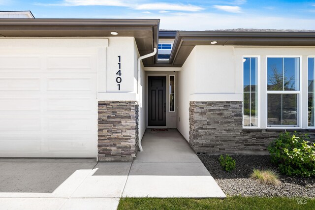 property entrance with an attached garage, stone siding, and stucco siding