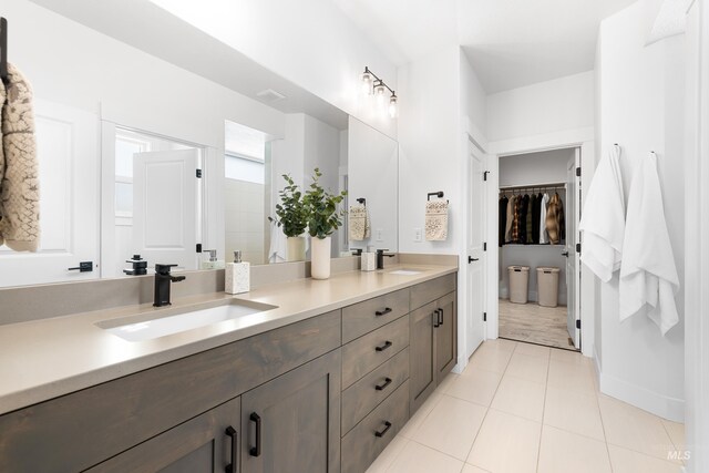 full bath with double vanity, a spacious closet, tile patterned flooring, and baseboards