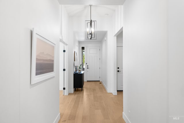 corridor featuring a chandelier, baseboards, and light wood-type flooring