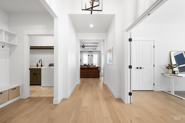 hallway with light wood-style flooring, baseboards, washer / clothes dryer, a sink, and recessed lighting