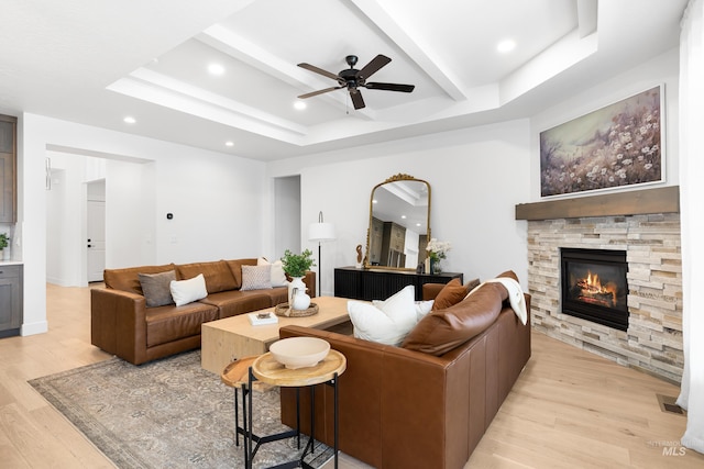 living room with light wood-type flooring, a ceiling fan, a tray ceiling, a fireplace, and recessed lighting
