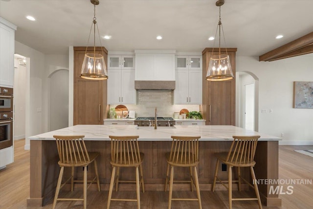 kitchen with a spacious island, arched walkways, decorative backsplash, custom range hood, and light wood-type flooring