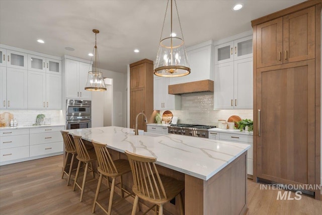 kitchen featuring glass insert cabinets, a breakfast bar area, custom range hood, light wood-style flooring, and stainless steel appliances