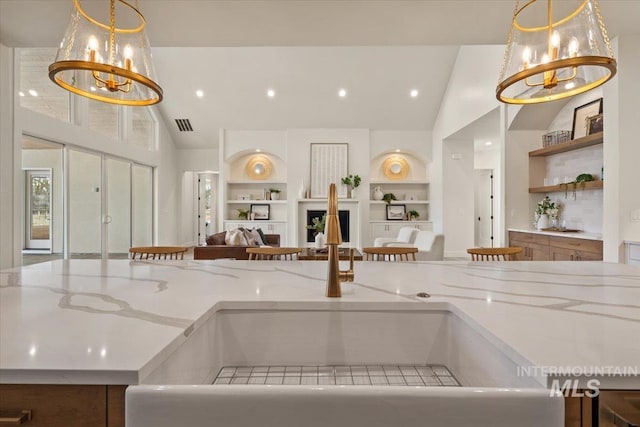 kitchen with built in features, open floor plan, light stone counters, and a chandelier