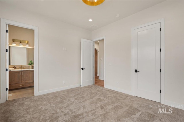 unfurnished bedroom featuring a sink, baseboards, light carpet, and arched walkways