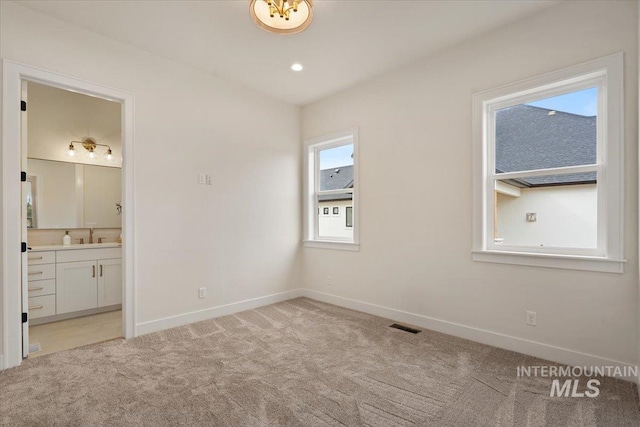 unfurnished bedroom with recessed lighting, baseboards, ensuite bathroom, and light carpet