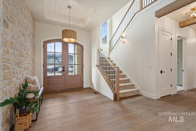 entrance foyer with stairs, a tray ceiling, french doors, wood finished floors, and arched walkways