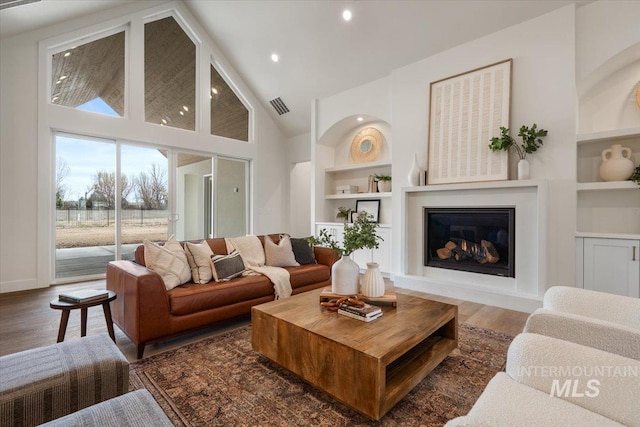 living area featuring visible vents, built in features, wood finished floors, a glass covered fireplace, and high vaulted ceiling