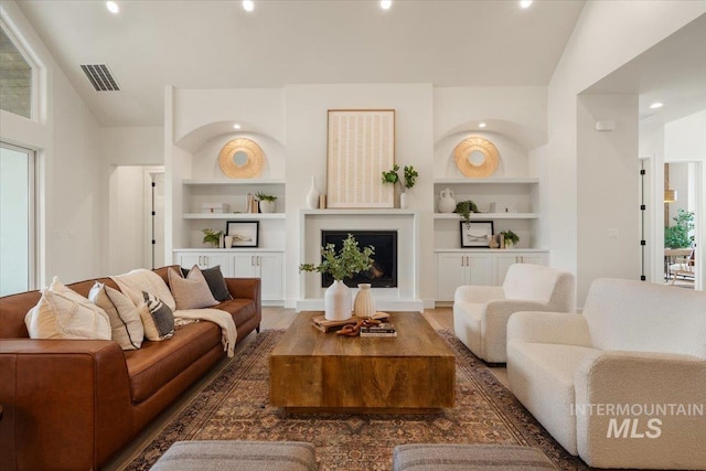 living area with visible vents, wood finished floors, lofted ceiling, and built in features