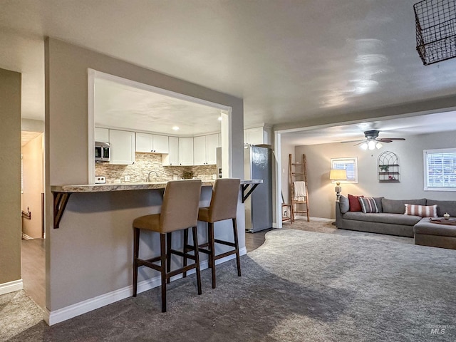 kitchen featuring carpet, white cabinets, a kitchen breakfast bar, appliances with stainless steel finishes, and kitchen peninsula