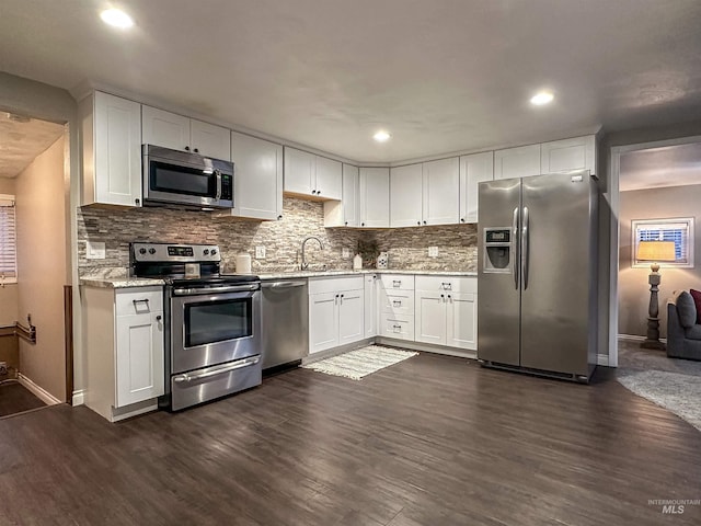 kitchen with dark wood-type flooring, light stone counters, decorative backsplash, white cabinets, and appliances with stainless steel finishes