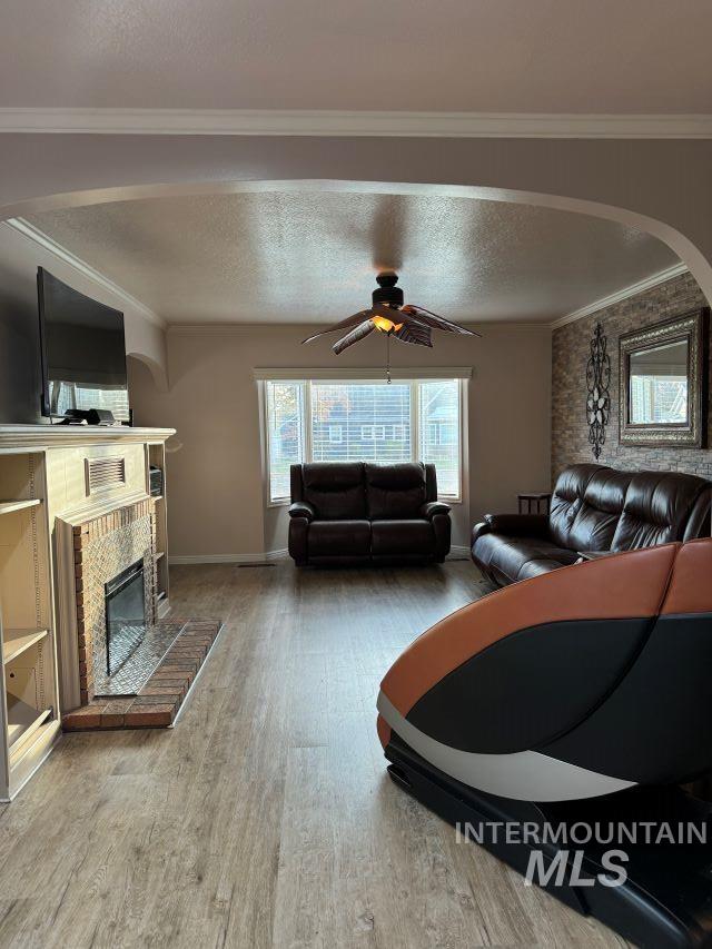 living room with hardwood / wood-style flooring, ornamental molding, a textured ceiling, and a brick fireplace