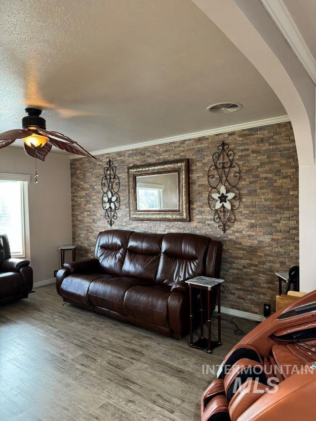 living room with hardwood / wood-style floors, ceiling fan, ornamental molding, and a textured ceiling