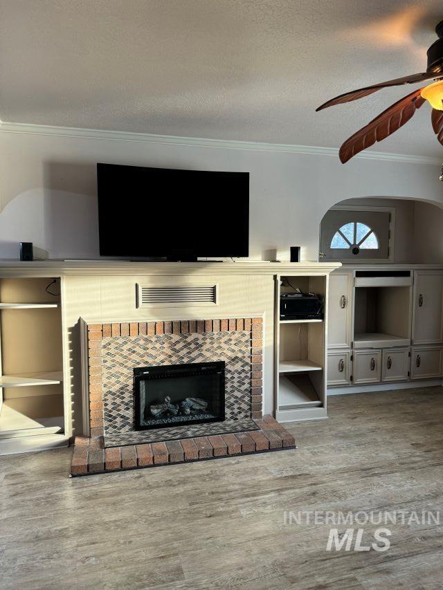 living room with ceiling fan, light hardwood / wood-style flooring, a textured ceiling, a fireplace, and ornamental molding