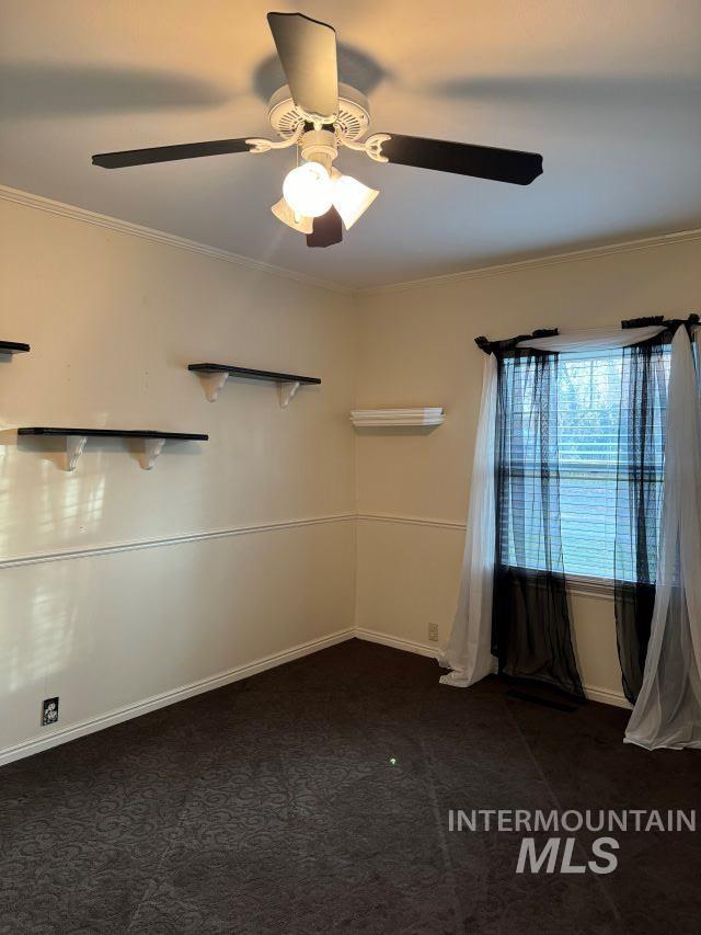 empty room with ceiling fan, dark colored carpet, and ornamental molding