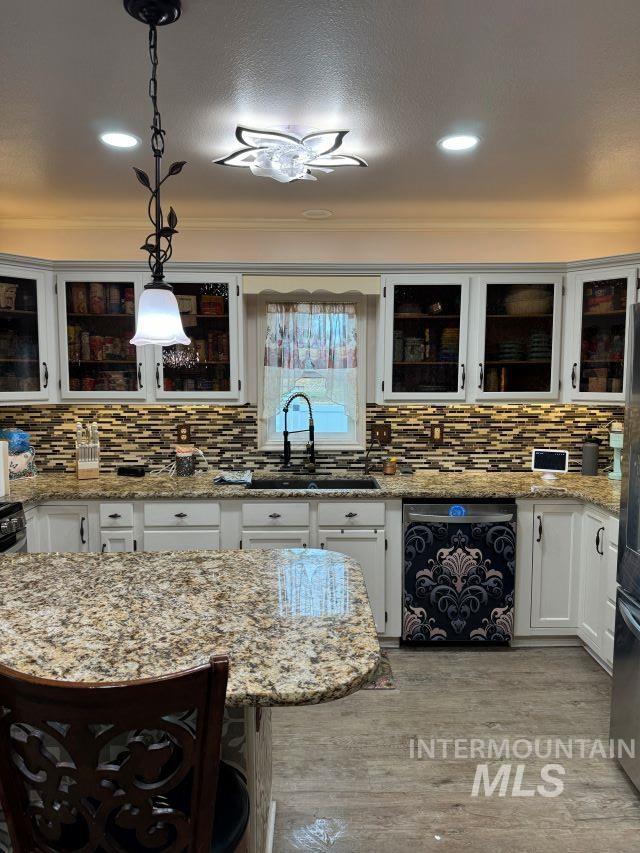 kitchen featuring pendant lighting, sink, light stone countertops, light wood-type flooring, and tasteful backsplash