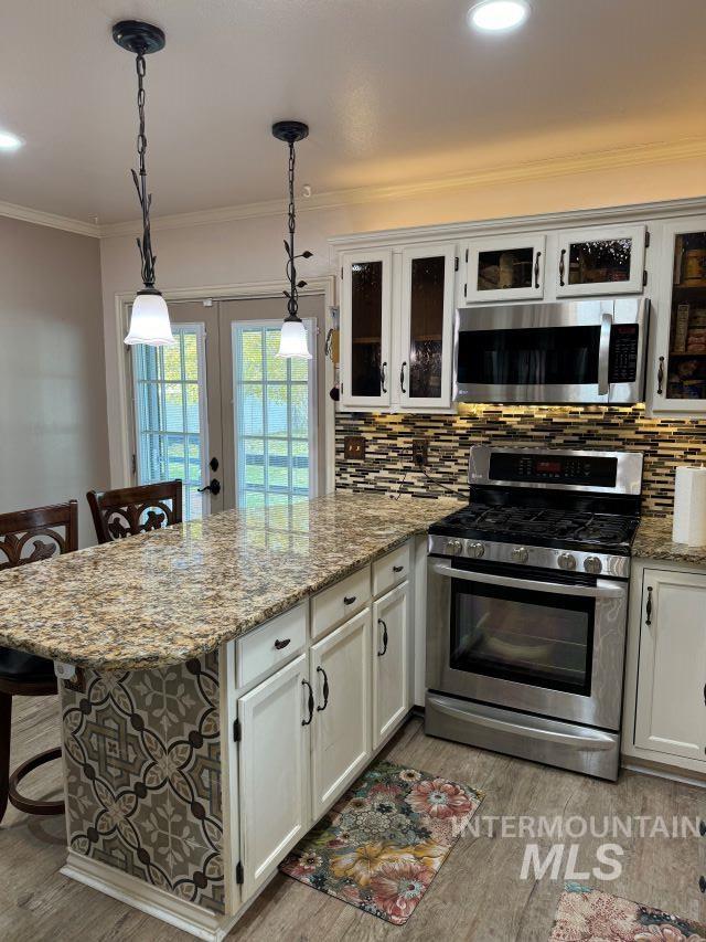 kitchen featuring light hardwood / wood-style floors, decorative light fixtures, a breakfast bar, white cabinets, and appliances with stainless steel finishes