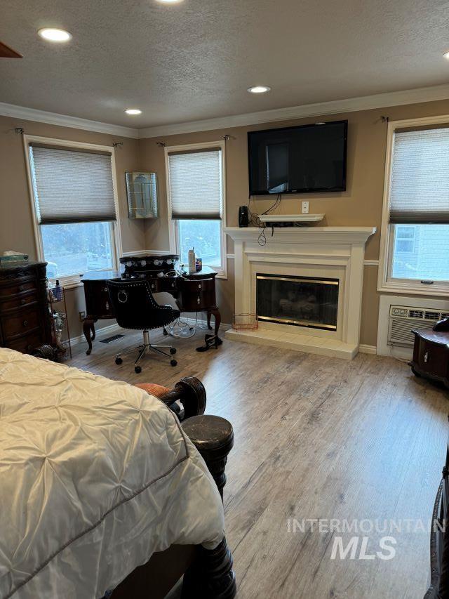 bedroom with hardwood / wood-style floors, a textured ceiling, a wall unit AC, and crown molding