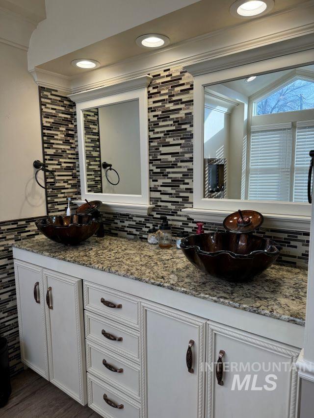 bathroom featuring wood-type flooring, vanity, crown molding, and backsplash