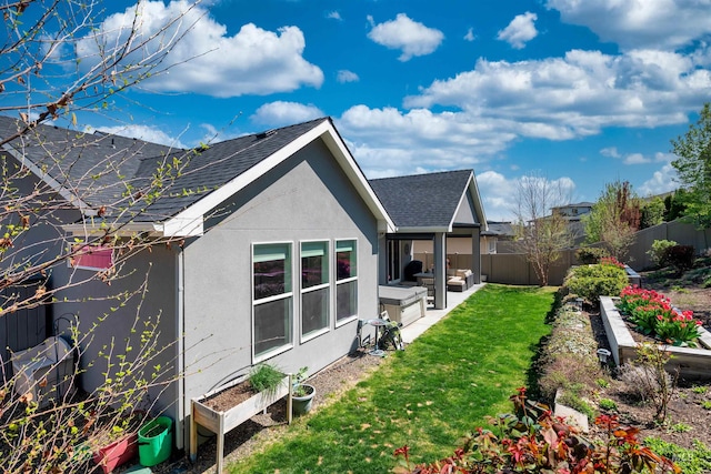 back of house featuring a garden, a shingled roof, a lawn, stucco siding, and fence private yard